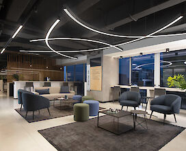 Moderne Büro-Lounge mit stilvollen Sitzgruppen und gebogenen LED-Licht an der Decke. Die Einrichtung umfasst blaue und graue Sessel sowie eine minimalistische Dekoration.