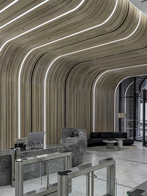 Bright lobby area with curved wooden panels, integrated LED lighting in the form of light lines and a modern glass entrance door.