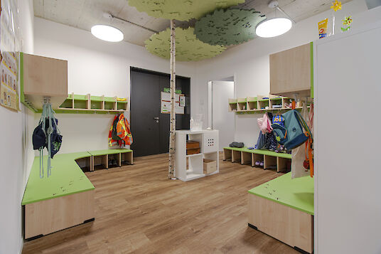 Cloakroom area with green benches, tree decor on the ceiling and round basic pendant luminaires.