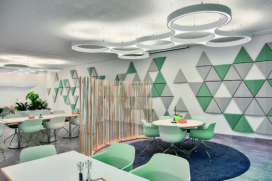 Kantine mit Akustikpaneelen, runden Tischen und ringförmigen Ringo Star Cluster Pendelleuchten.