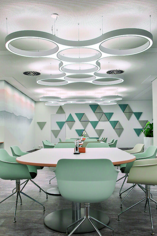 Kantine mit großen runden Tischen, gepolsterten Stühlen und Ringo Star Cluster Pendelleuchten.