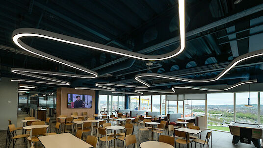 Canteen with organically curved Liquid Line ceiling lighting and large window fronts.