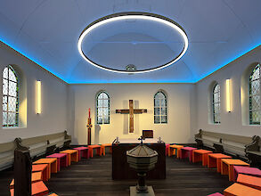 Moderna capilla iluminada con un gran anillo luminoso y coloridos taburetes en semicírculo