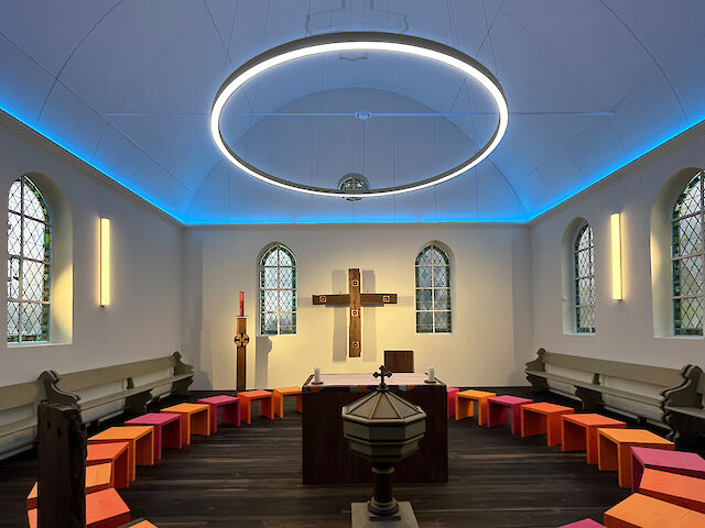 Chapelle éclairée de façon moderne avec un grand anneau lumineux et des tabourets colorés en demi-cercle