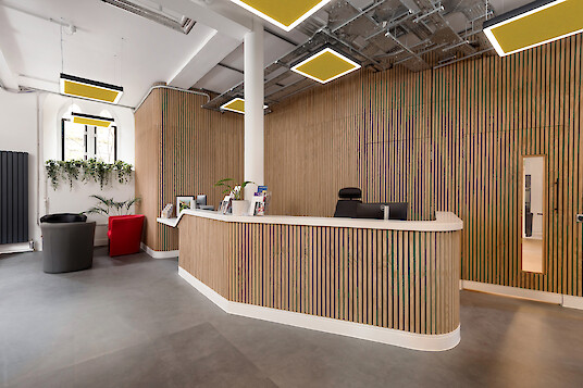 Espace d'accueil avec des lamelles en bois, un comptoir, des sièges et des suspensions carrées dotées de panneaux acoustiques