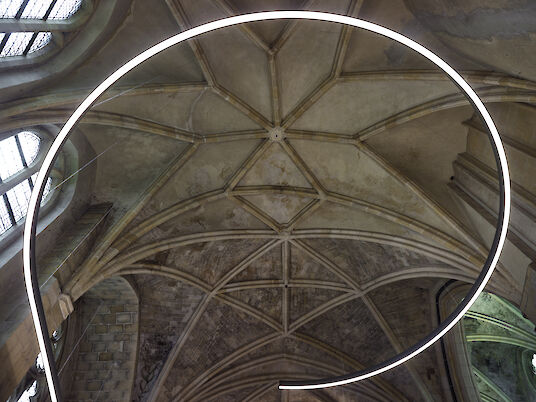 Línea de luz curva en forma de anillo delante de una bóveda gótica, vista desde abajo.