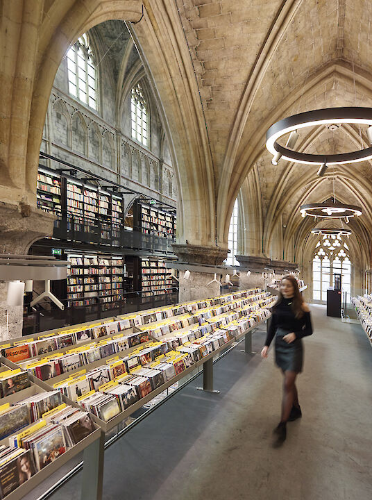Librería en una iglesia gótica con bóvedas altas y luminarias suspendidas Ringo Star en forma de anillo.