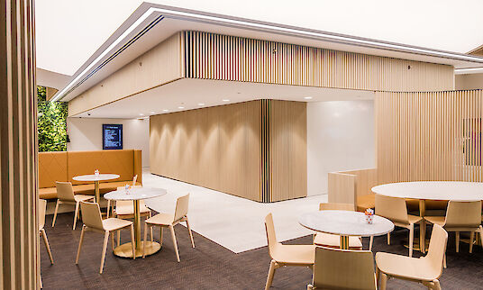 Cafetería con mobiliario de madera clara, mesas redondas e iluminación LED en el techo con líneas de luces empotradas Matric.