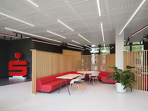 Moderne Lounge der Berliner Sparkasse mit roten Sitzbänken, Holzelementen und linearen LED-Leuchten