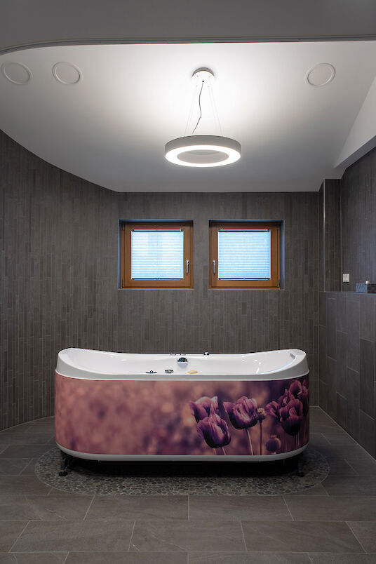 Bathroom with bathtub, ring-shaped Ringo Star pendant luminaire and floral motif panelling in purple.