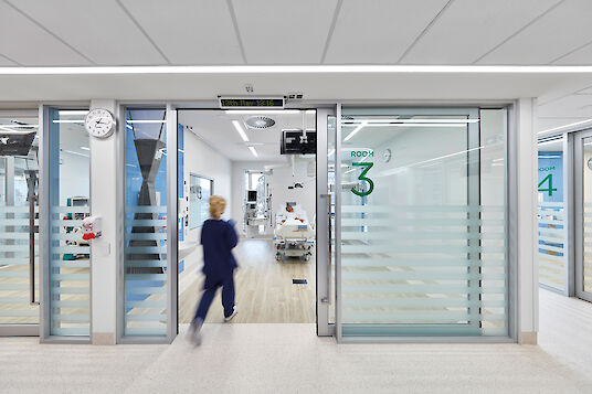 Chambre du patient visible à travers une façade vitrée avec désignation de la chambre, personnel soignant, lignes lumineuses Matric.
