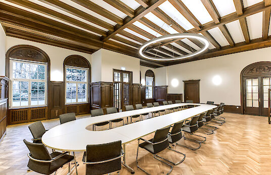 Konferenzraum mit Holzdecke, U-förmigem Tisch, Stühlen und Ringo-Star-Pendelleuchte.