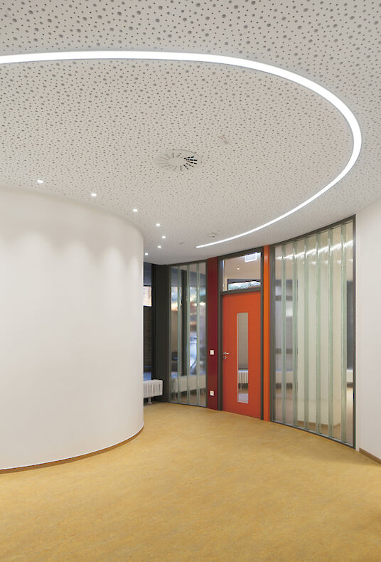 Couloir avec sol jaune, mur incurvé et ligne lumineuse encastrée Liquid Line dans un plafond perforé.