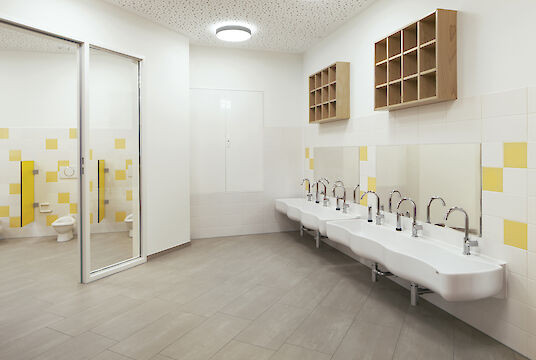 Salle de bain pour enfants avec lavabo à hauteur d'enfant, carrelage jaune et blanc et luminaire Basic rond apparent au plafond.