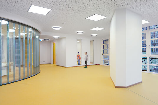 Enfants dans une pièce lumineuse avec un sol jaune, de grandes baies vitrées et des plafonniers carrés Cubic.