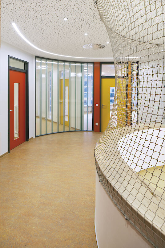 Espace avec structure réticulée, portes colorées, parois en verre et ligne lumineuse encastrée Liquid Line incurvée dans le plafond.