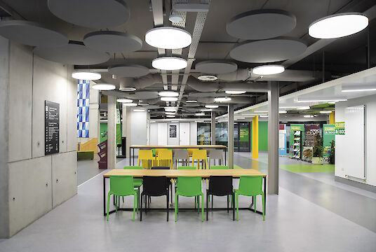 Lounge area with colourful chairs, round Basic pendant luminaires and suspended acoustic elements.