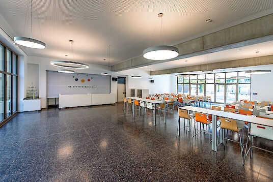Large dining room with white walls, colourful chairs and Ringo Star and basic pendant luminaires.