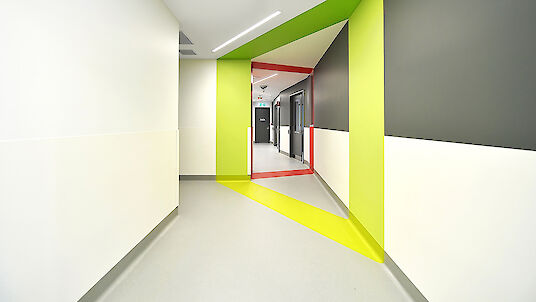 Hallway with graphic colour surfaces in yellow and red and linear Matric recessed luminaires.