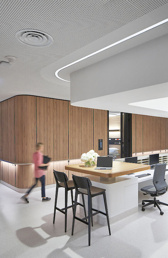 Reception desk with wooden panelling, Liquid Line light line and person walking past in the hospital.