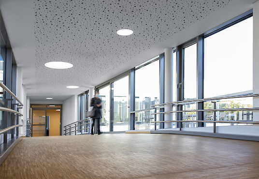 Bright transition with large windows, wooden floor, handrails and round Basic ceiling luminaires.
