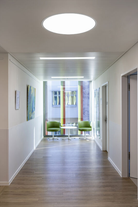 Bright hallway with wooden flooring, round Basic recessed luminaire and waiting area by the window.