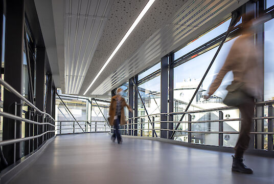 Covered crossing with glass façade, handrails, Matric recessed luminaire and people walking.