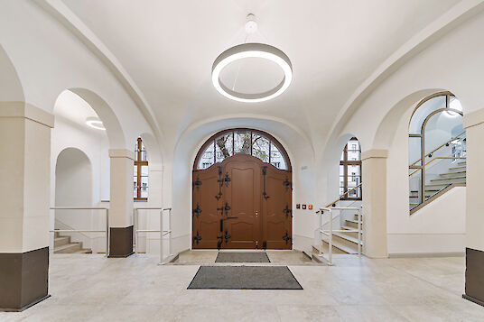 Historic entrance area with round arches, wooden portal and ring-shaped Ringo Star pendant luminaires.