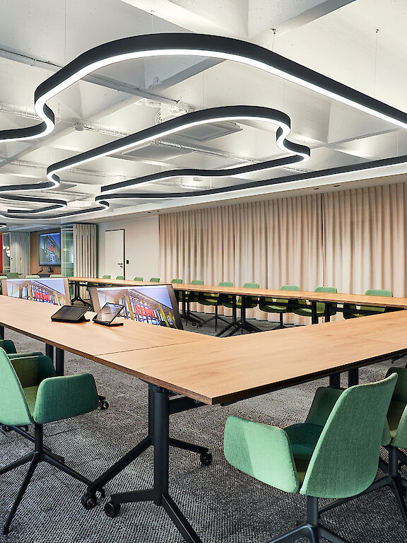 Large conference room with green chairs and curved Liquid Line lighting on the ceiling.
