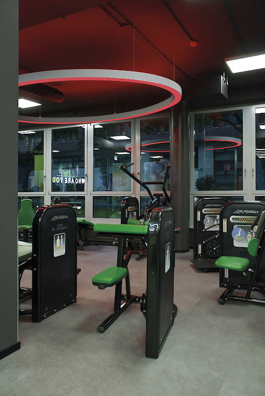 Gym with green training equipment and red Ringo Star pendant luminaire above a grey floor.