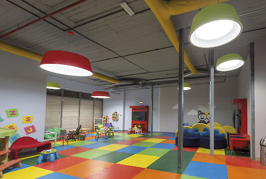 Colorida zona infantil con suelo de colores, muebles de juego y grandes luminarias suspendidas redondas Beam Me Up.