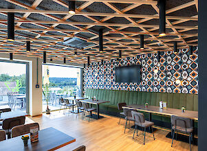 Modern restaurant interior with wooden ceiling, geometric pattern, large windows and midpoint lights for warm light.