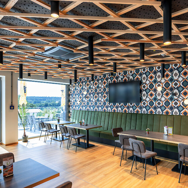 Modern restaurant interior with wooden ceiling, geometric pattern, large windows and midpoint lights for warm light.