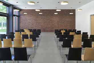 Moderner Veranstaltungsraum mit schwarzen und holzfarbenen Stühlen, Ziegelwand und runden Pendelleuchten.