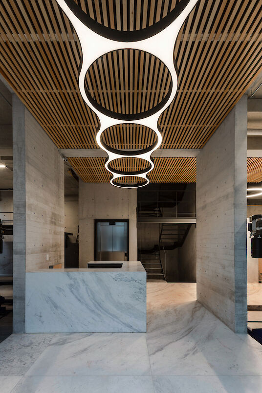 Bright living room with large window fronts, plants, dining table and rectangular pendant lights on concrete ceiling