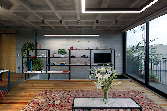 Living room with large shelving unit, exposed concrete wall, rectangular pendant lights and view of the balcony