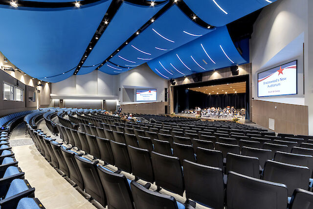 Auditorium with curved blue ceiling panels, integrated light lines and black seating area.