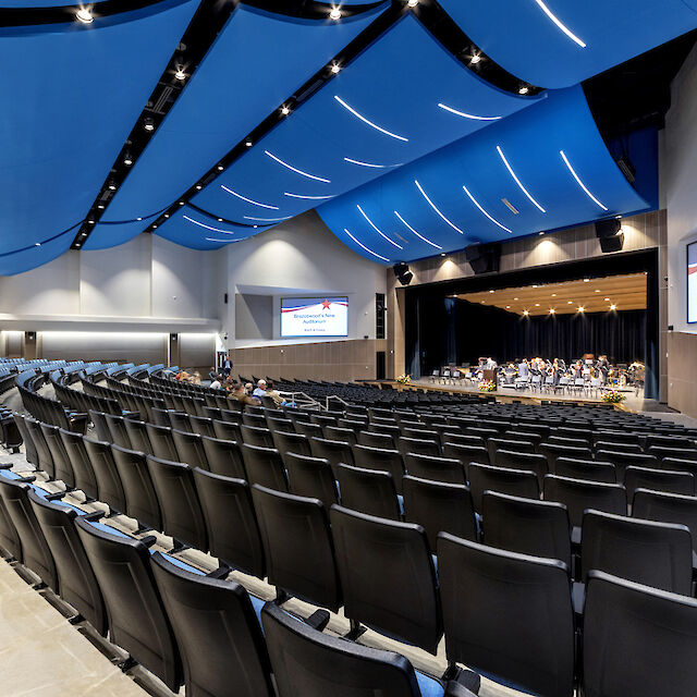 Auditorium mit gebogenen blauen Deckenpaneelen, integrierten Lichtlinien und schwarzem Bestuhlungsbereich.