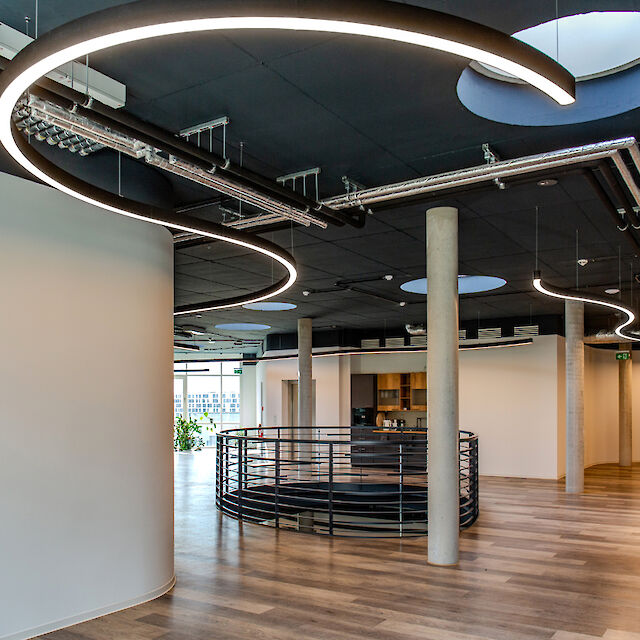 Geschwungene Liquid Line LED-Pendelleuchten strukturieren ein modernes, offen gestaltetes Bürointerieur.