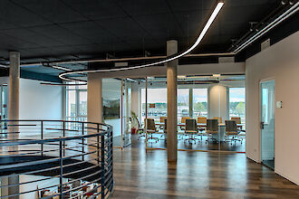 Fließende LED-Linienleuchte führt durch ein modernes Büro mit Glas-Konferenzraum und Tageslichteinfall.