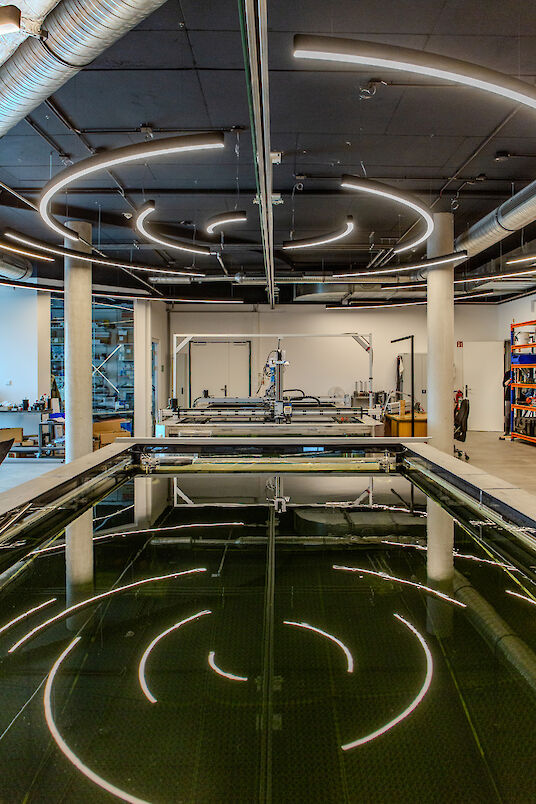 Geschwungene Liquid Line LED-Lichtlinien an schwarzer Decke spiegeln sich in großem Wasserbecken.