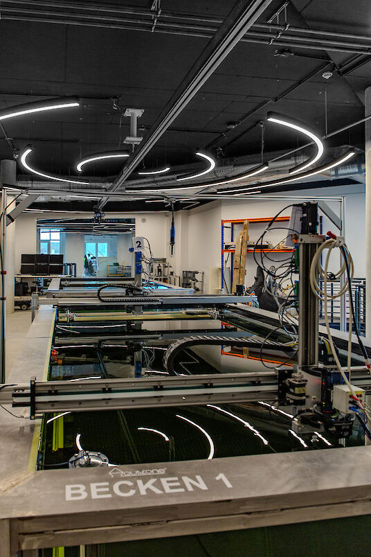 Geschwungene LED-Lichtlinien der Serie Liquid Line spiegeln sich über einem großen Technikbecken mit Beschriftung.