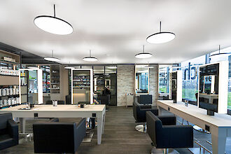 Modern hairdressing salon with illuminated mirrors, black armchairs and large windows overlooking the street