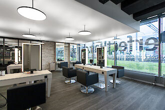 Bright hairdressing salon with large windows, black armchairs and illuminated mirrors at white tables