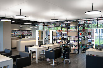 Modern hairdressing salon with black armchairs, illuminated mirrors and ceiling-mounted round pendant lights