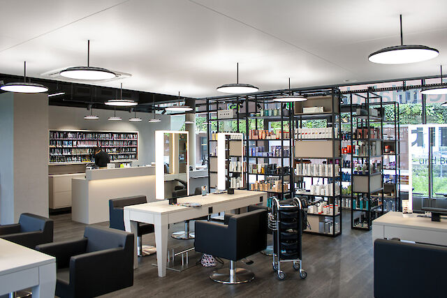 Modern hairdressing salon with black armchairs, illuminated mirrors and ceiling-mounted round pendant lights