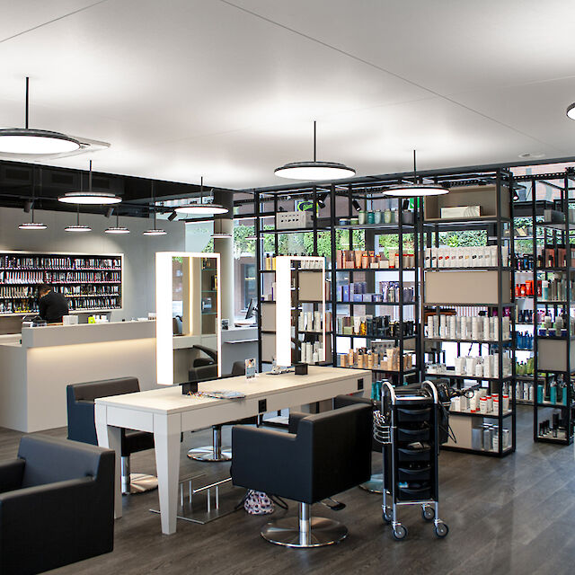 Modern hairdressing salon with black armchairs, illuminated mirrors and ceiling-mounted round pendant lights