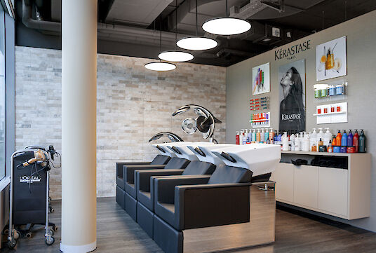 Wash area in the hairdressing salon with black chairs, white basin and illuminated product wall