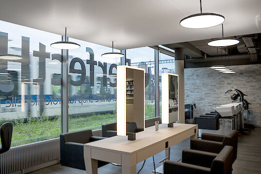 Modern hairdressing salon with large windows, illuminated mirrors and washing areas in front of a brick wall