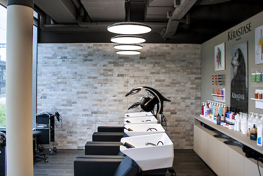 Wash area in the hairdressing salon with white basins, black chairs and product shelves on the wall